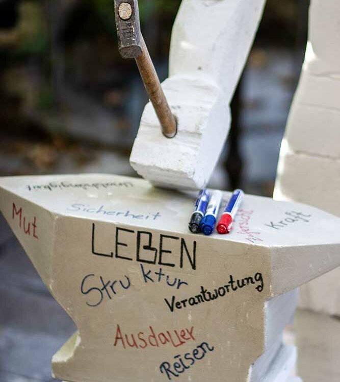 Skulptur mit Symbolik: Ein aus YTON gefertigter Amboss wird von einem YTON-Mann mit einem Hammer geschlagen