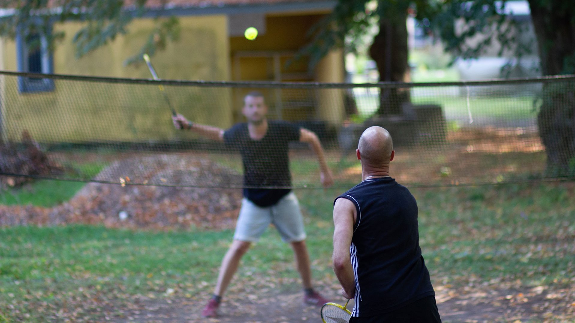 Sport-Szene im Garten: zwei Männer in Sportoutfit spielen Badminton