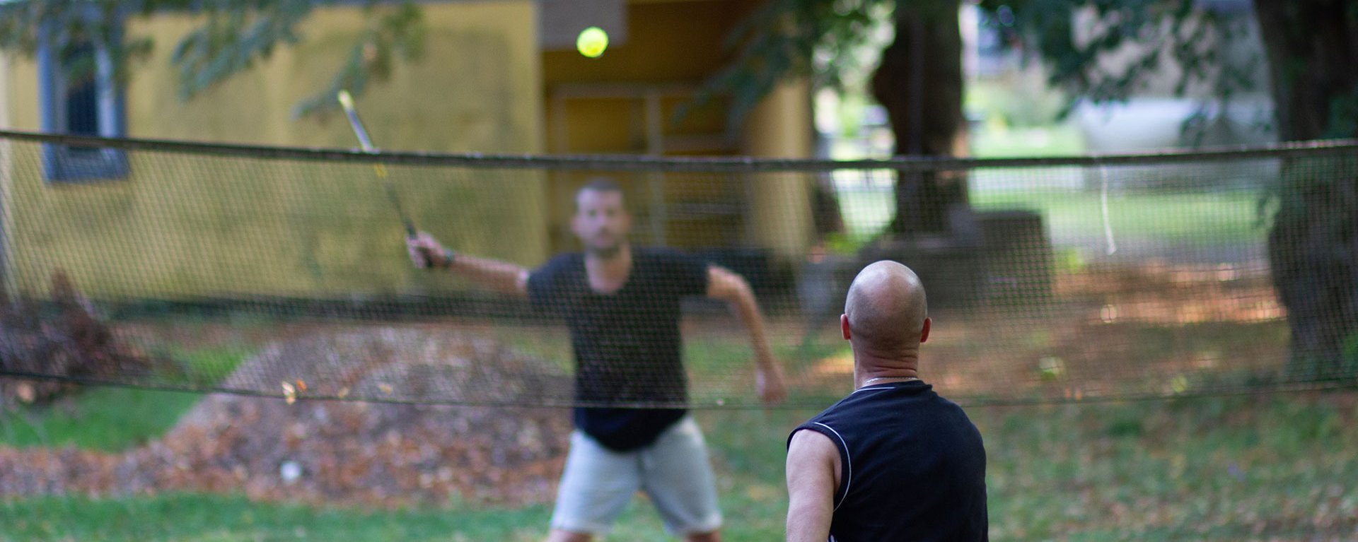 Sport-Szene im Garten: zwei Männer in Sportoutfit spielen Badminton