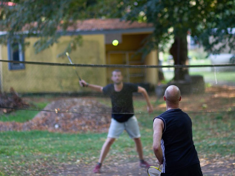 Sport-Szene im Garten: zwei Männer in Sportoutfit spielen Badminton