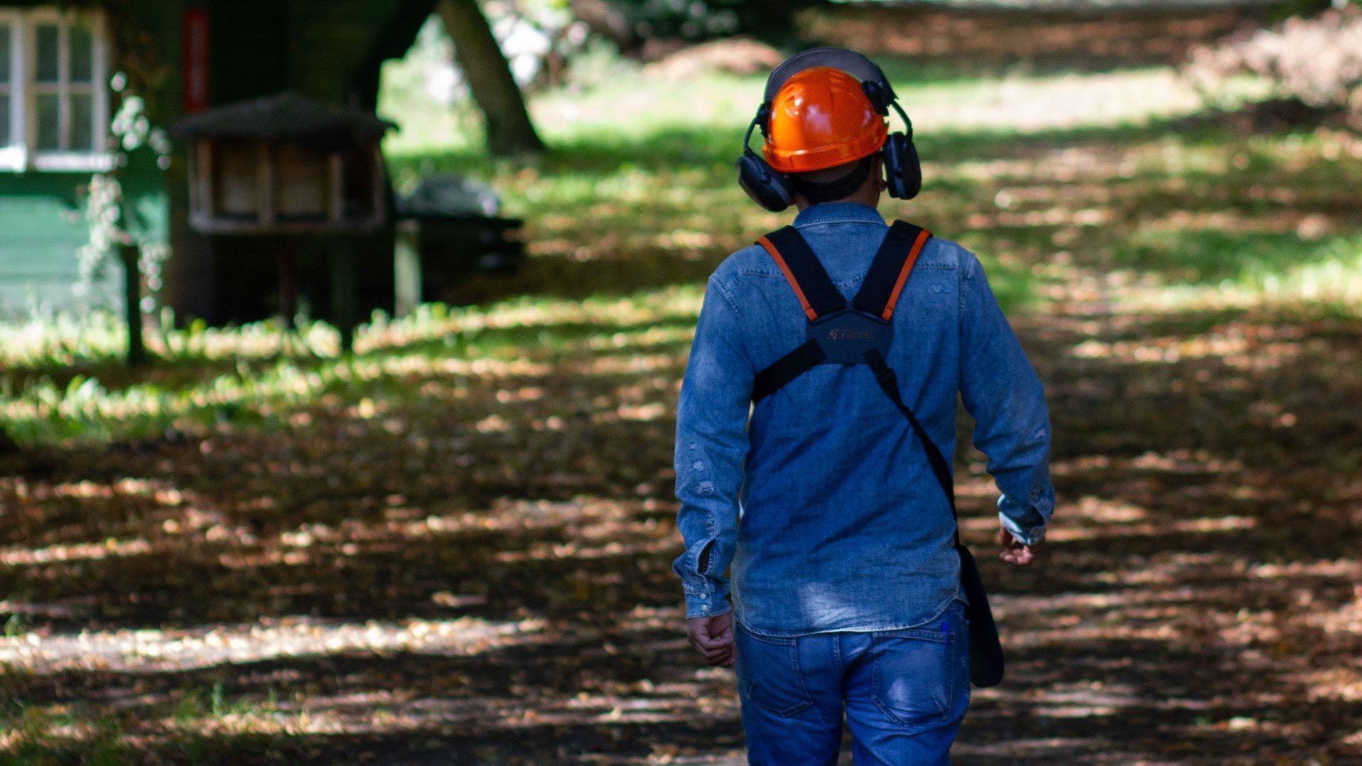 Gartenarbeit: ein Mann mit Arbeitssicherheits-Ausrüstung und orangem Helm geht durch den Garten